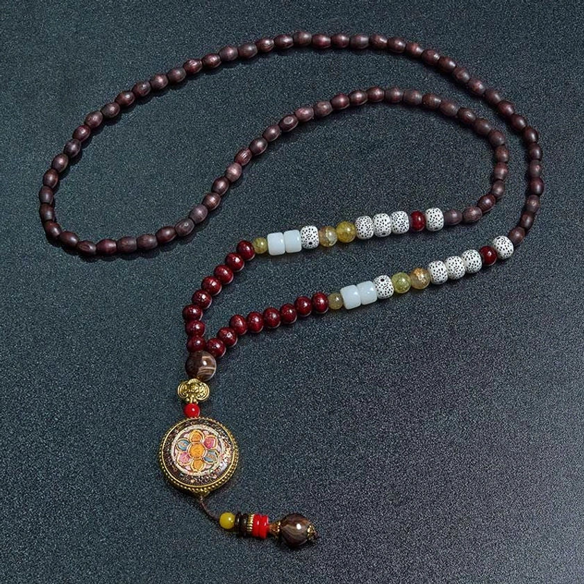 Buddhist mala necklace with white and metallic spacer beads, enamel pendant on dark background