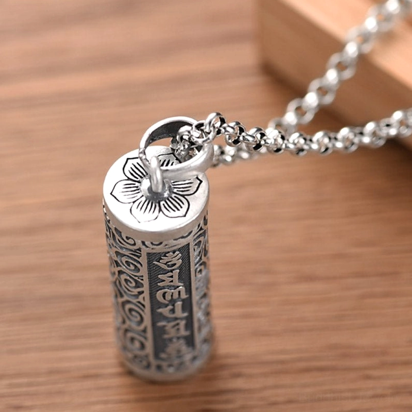 Buddhist mantra pendant necklace overhead view - full engraved pattern details with linked silver chain on light background