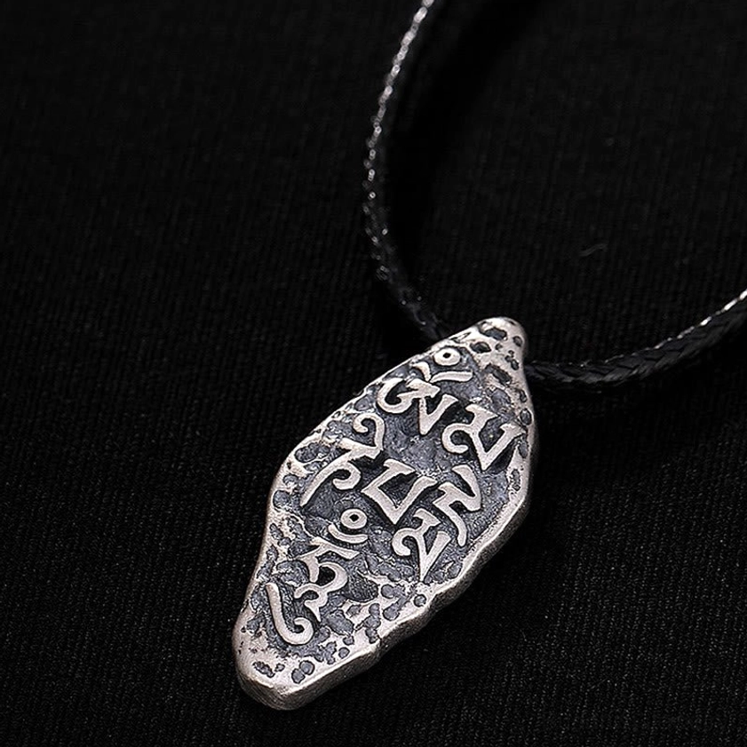 Om Mani Padme Hum necklace presentation view, sterling silver pendant on black leather cord displayed on wooden surface