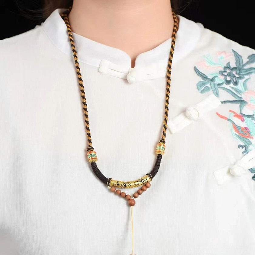 Handmade Buddhist prayer necklace worn on person with traditional embroidered shirt, showing braided cord and religious metal decoration