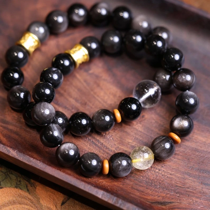 Two matching Silver Sheen Obsidian Buddhist protection bracelets displayed on wooden tray with crystal and wooden spacers