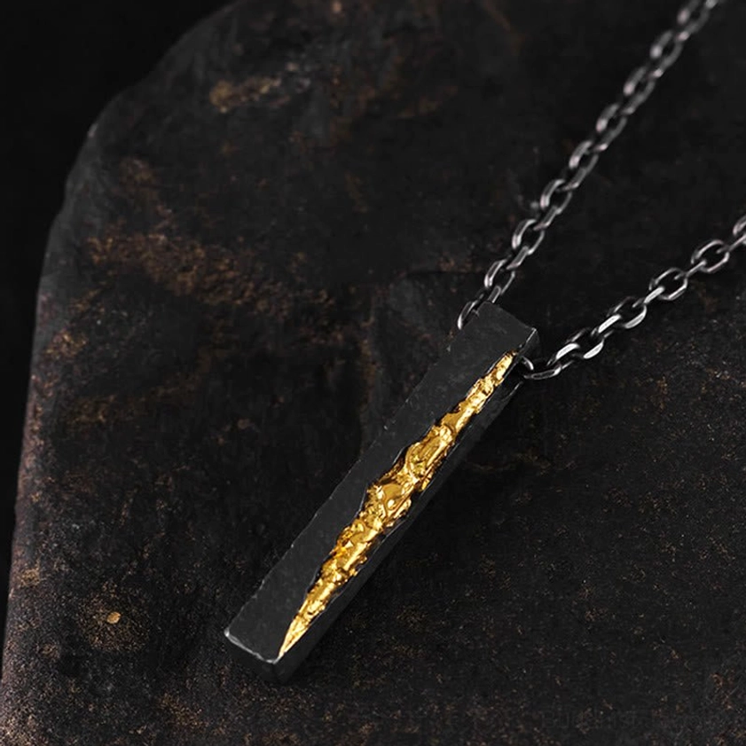 Buddhist Om Mani Padme Hum necklace pendant hanging, oblique low side view on dark stone background showing mantra bar design and chain attachment