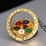 Om Mani Padme Hum gold-plated phone ring holder with lotus embossed design, displayed on desk showing six-syllable mantra enamel craft