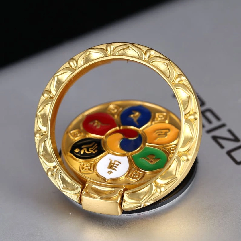Om Mani Padme Hum gold-plated phone ring holder with lotus embossed design, displayed on desk showing six-syllable mantra enamel craft