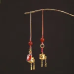 Om Mani Padme Hum prayer wheel charm with multicolored braided cord and red agate beads displayed on dark background