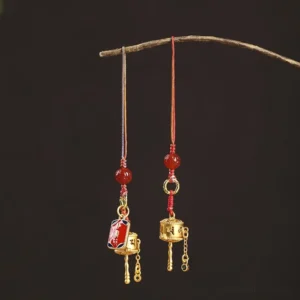 Om Mani Padme Hum prayer wheel charm with multicolored braided cord and red agate beads displayed on dark background