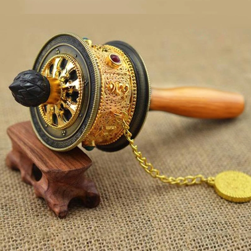 Single Buddhist prayer wheel in gold and black finish with polished wood handle and silver hanging chain pendant, displayed on wooden stand