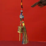 Antique bronze Om Mani Padme Hum prayer wheel keychain with colorful tassels hanging on wooden branch display