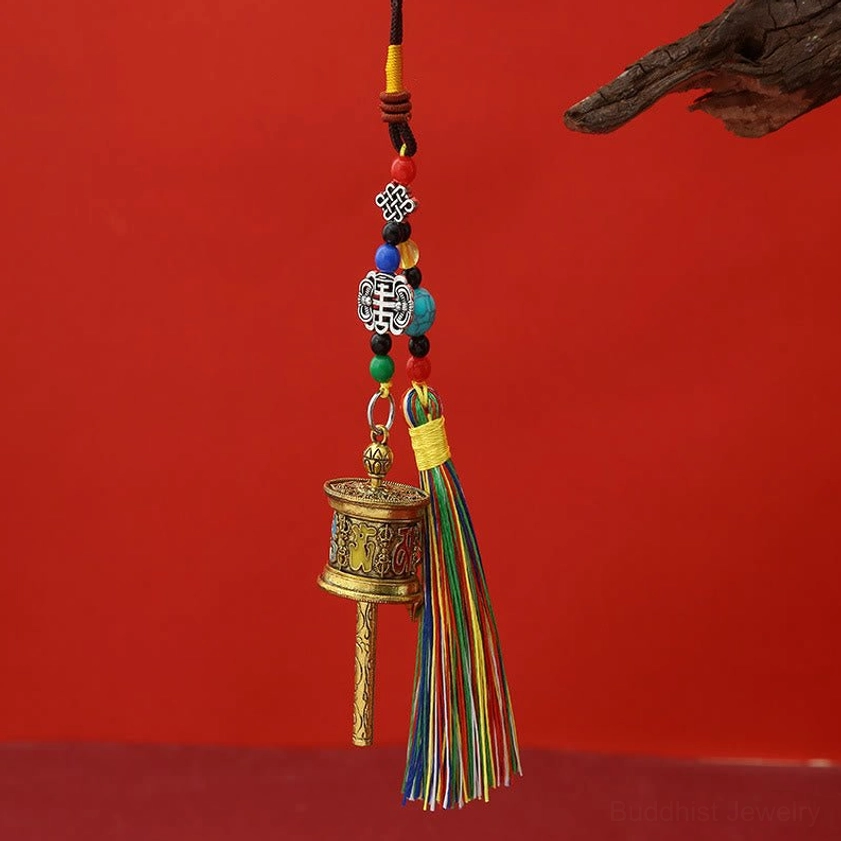 Antique bronze Om Mani Padme Hum prayer wheel keychain with colorful tassels hanging on wooden branch display
