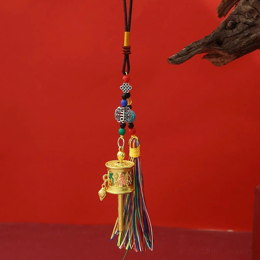 Polished gold finish Om Mani Padme Hum prayer wheel keychain with multicolored tassels displayed on red background