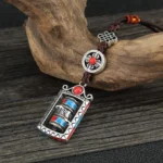 Om Mani Padme Hum prayer wheel keychain with rotatable cylinder and silver metal frame on wooden surface