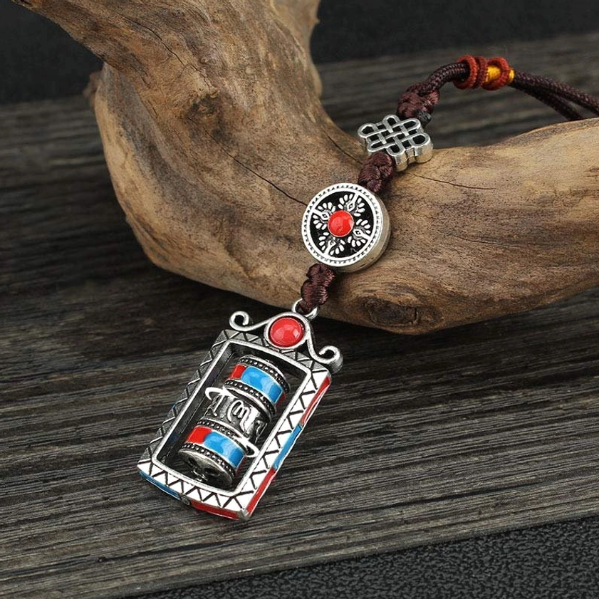 Om Mani Padme Hum prayer wheel keychain with rotatable cylinder and silver metal frame on wooden surface
