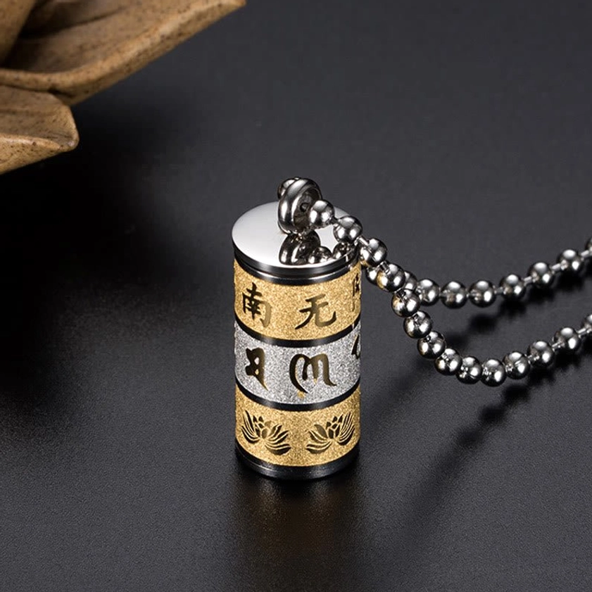 Close-up oblique side view of Om Mani Padme Hum prayer wheel pendant showing three-tone layered surface, screw-on sealed cap, and detailed lotus flower engraving against dark background