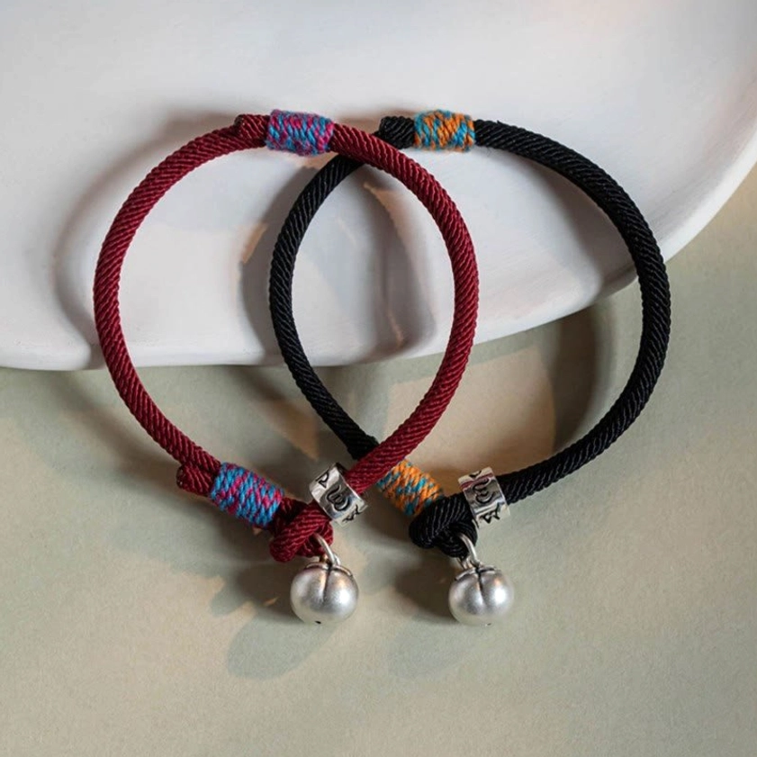 Red and black Buddhist string bracelets with silver charms displayed together on gray ceramic plate