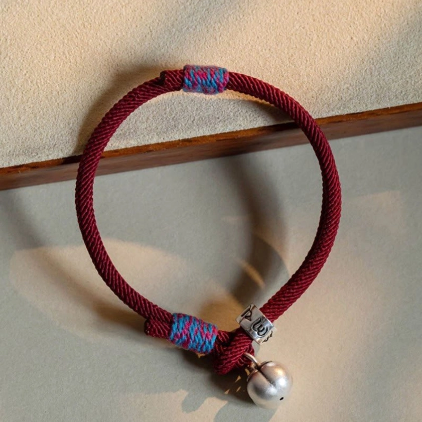 Wine red braided Buddhist lucky bracelet with sterling silver mantra charm and persimmon bell on wooden tray