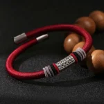 Red string bracelet with 925 sterling silver Om Mani Padme Hum charm, close-up with wooden prayer beads