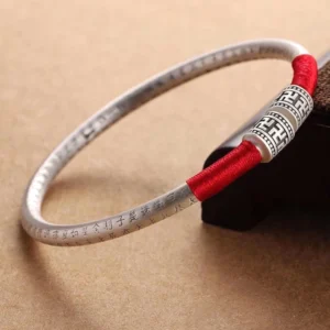 Om Mani Padme Hum red string bracelet with engraved silver charm, overhead close-up view on brown wooden display