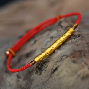 Om Mani Padme Hum red string bracelet with gold-plated sterling silver charm, overhead view on wooden texture background