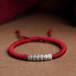 Handmade sterling silver Om Mani Padme Hum dark red rope bracelet with engraved blessing charm on wooden table