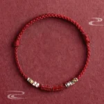 Om Mani Padme Hum red string bracelet with sterling silver cinnabar beads, flat lay overhead view showing braided cord and colorful knots