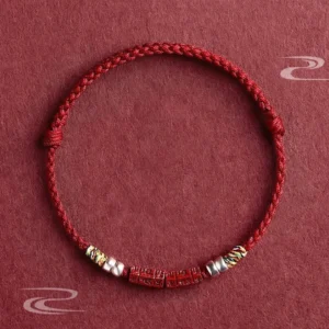 Om Mani Padme Hum red string bracelet with sterling silver cinnabar beads, flat lay overhead view showing braided cord and colorful knots