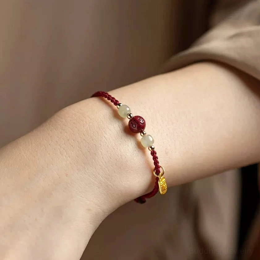Red string Hetian jade bracelet worn on wrist showing Fu charm and cinnabar bead