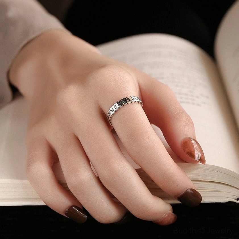 Om Mani Padme Hum sterling silver ring worn on hand - lifestyle shot showing proper fit on index finger over book background