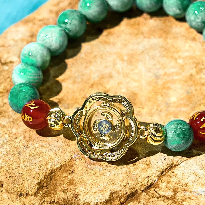 Rotating cyclone charm bracelet with green marbled jade beads and engraved agate on stone surface