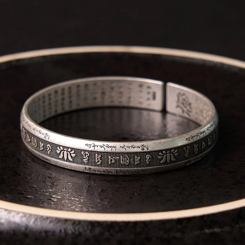 Buddhist mantra silver cuff with inner full text engraving and lotus motif, top-down view on dark glossy plate