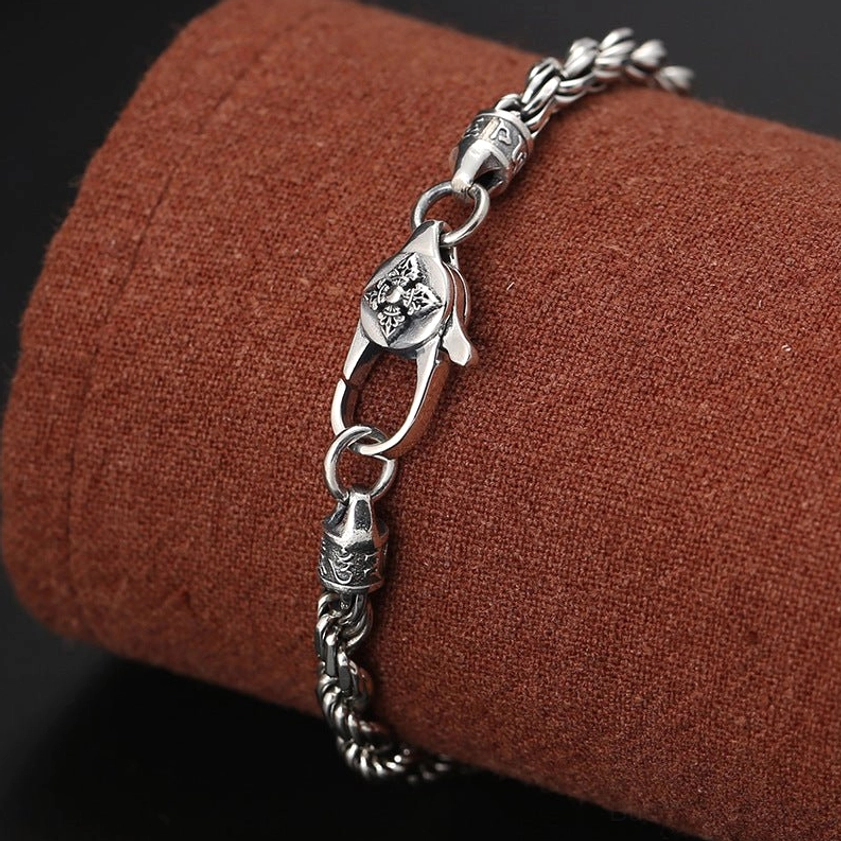 Om mani padme hum double dorje vajra silver bracelet on brown fabric display showing carved lobster clasp and twisted texture