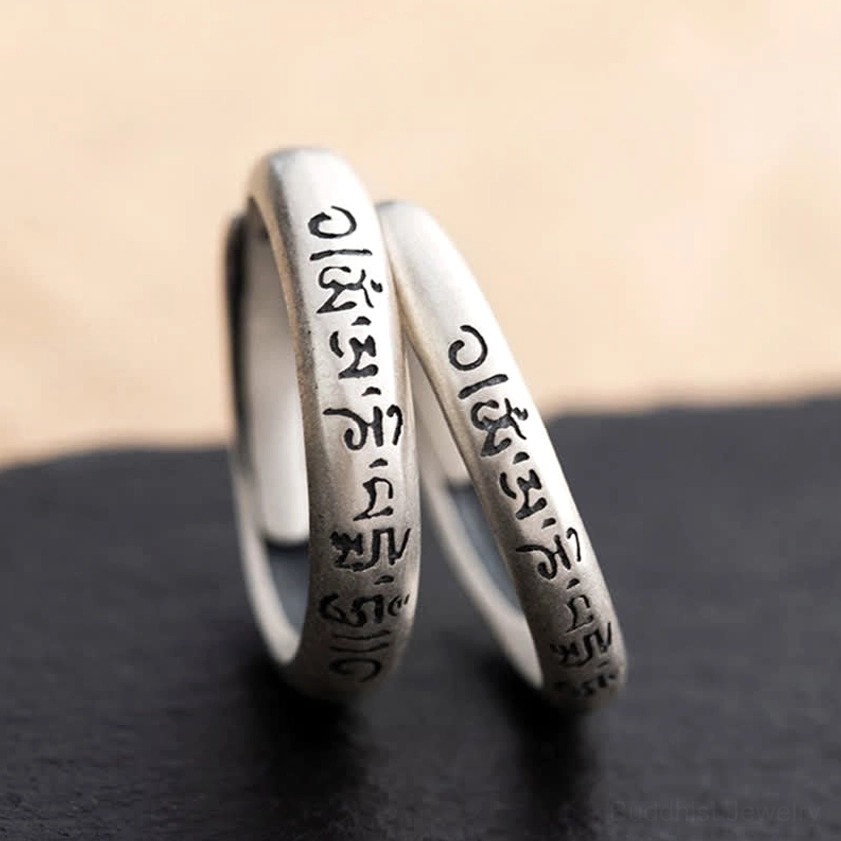 Pair of Om Mani Padme Hum sterling silver Buddhist rings placed parallel on dark surface showing matte finish