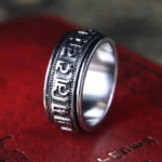 Om Mani Padme Hum titanium steel spinner ring with engraved Sanskrit mantra, three-quarter view on vintage book background