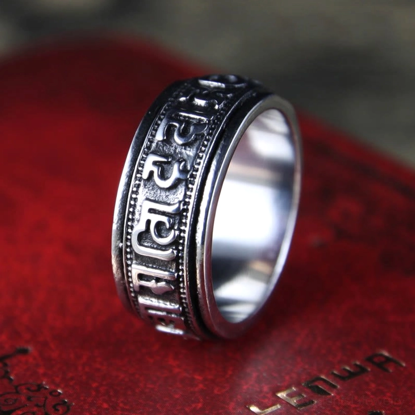 Om Mani Padme Hum titanium steel spinner ring with engraved Sanskrit mantra, three-quarter view on vintage book background