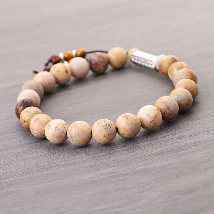 Flat lay of weathered stone Buddhist bracelet featuring round matte beads, metal mantra charm, and adjustable tassel