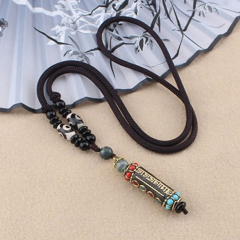 Buddhist string cord necklace with enamel inlaid mantra charm and dzi bead, black cord style flat lay
