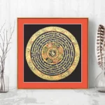 Hand-painted Buddhist thangka scroll with Om Mani Padme Hum mantra in gilded mandala design on black background, displayed in minimalist living room with red frame