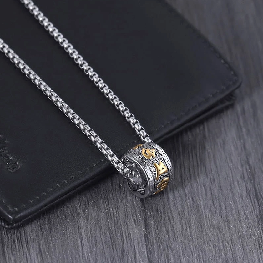 Two-tone Om Mani Padme Hum pendant necklace with gold accents, side view on wooden surface near leather accessories