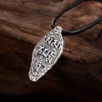 Om Mani Padme Hum Vajra silver pendant on dark wooden background, showing engraved Tibetan script with vintage silver finish, upper left oblique angle