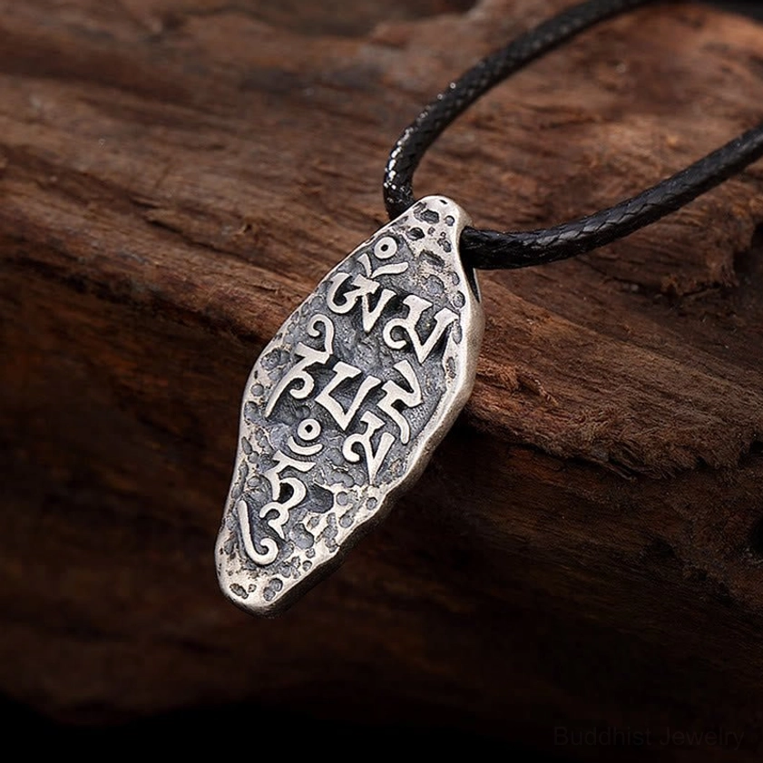 Om Mani Padme Hum Vajra silver pendant on dark wooden background, showing engraved Tibetan script with vintage silver finish, upper left oblique angle