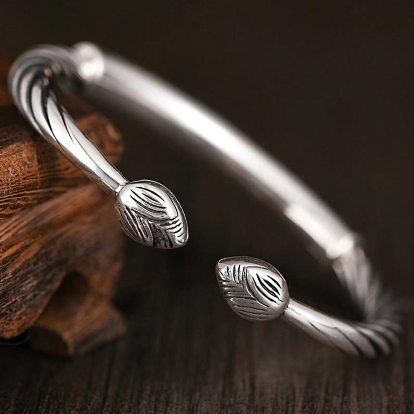 Vintage-style Buddhist scripture cuff bracelet with full engraved Om Mani Padme Hum text, twisted rope band, and rounded end caps on dark wood surface