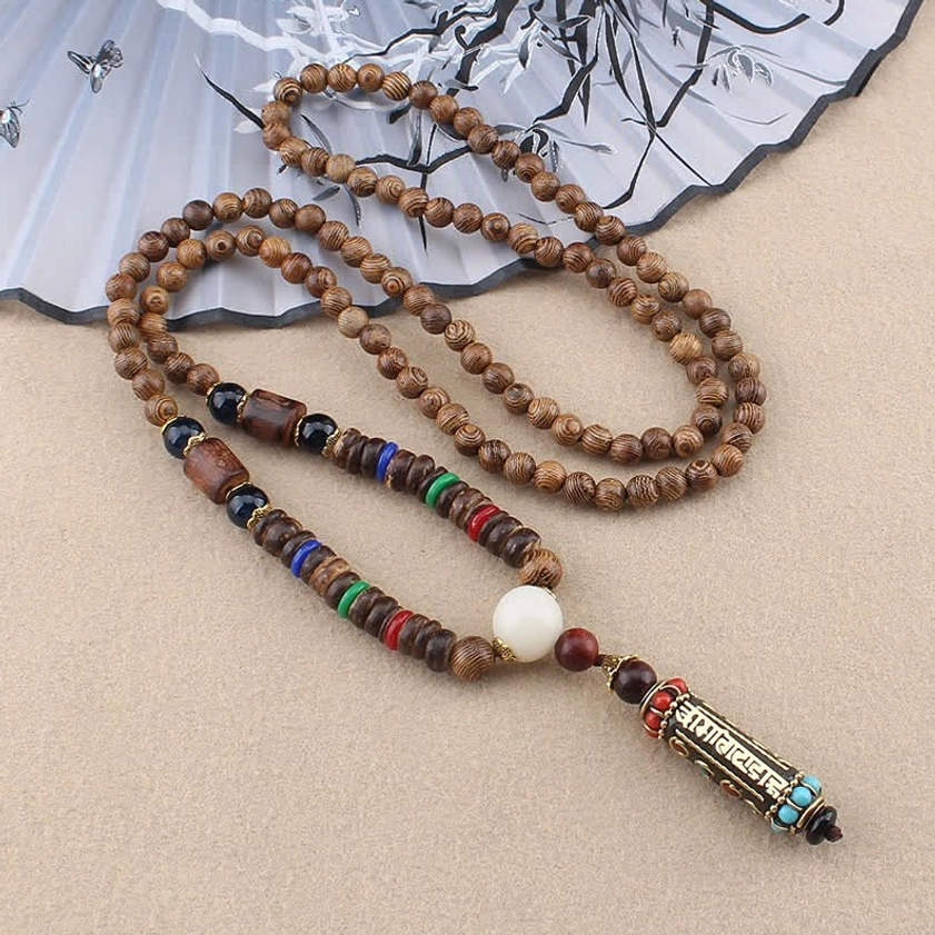 Om Mani Padme Hum Buddhist necklace with wenge wood beads and metal mantra pendant displayed on traditional ink painting fan, overhead view