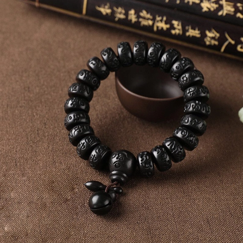 Buddhist wooden protection bracelet with matte black script-carved mantra beads and wooden bell pendant, calligraphy background