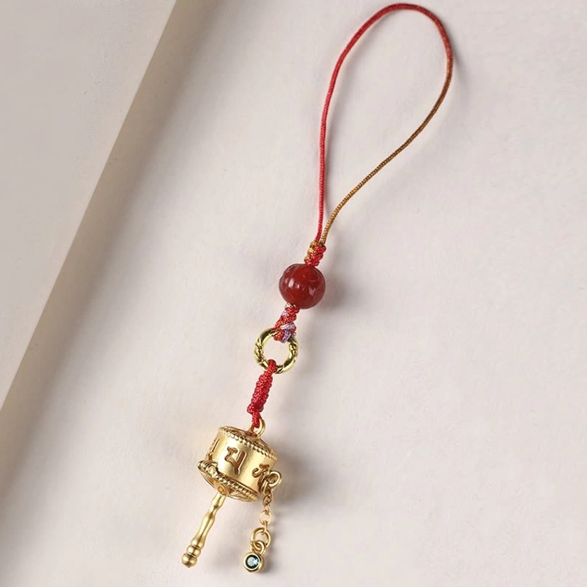 Buddhist prayer wheel phone charm with red-gold braided cord and Sanskrit pattern prayer wheel on book