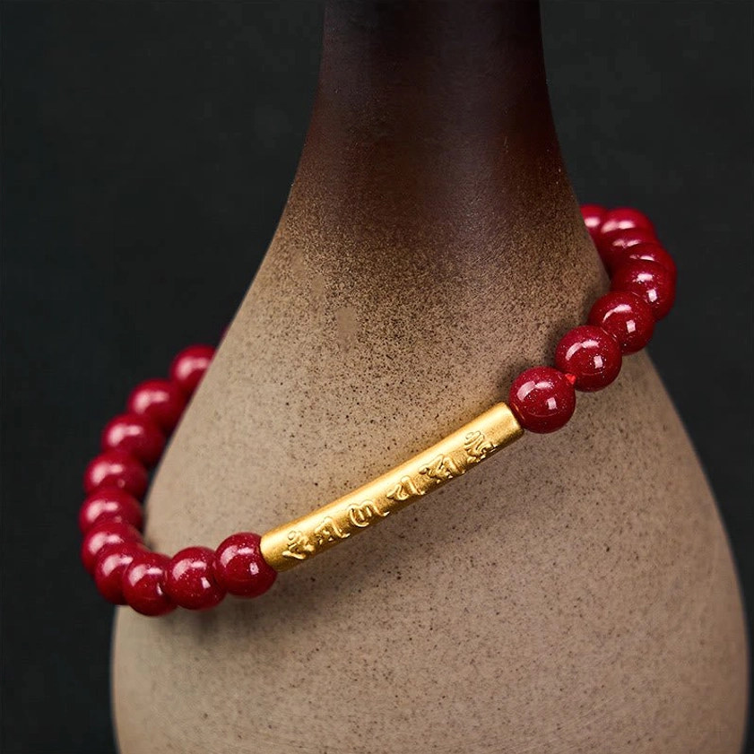 Om Mani Padme Hum cinnabar bracelet wrapped around ceramic vessel, displaying polished red beads and engraved silver tube close-up