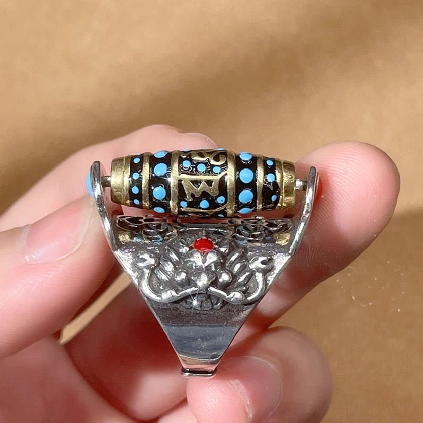 Rotatable Dzi bead Buddhist ring held on finger showing rear view with red gem inlay and Garuda relief