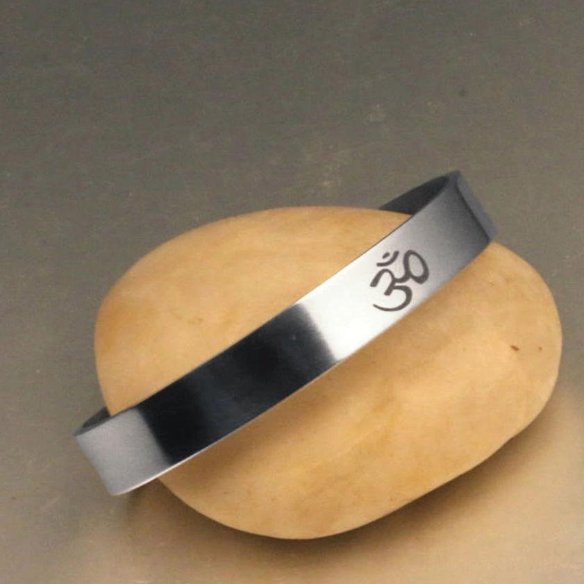 Mindfulness OM cuff bracelet with brushed silver finish, low side angle on yellow stone background