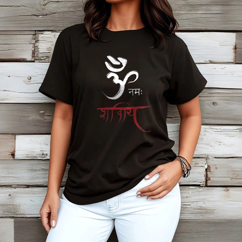 Woman wearing black Om Namah Shivaya Sanskrit tee paired with white pants, wooden wall setting
