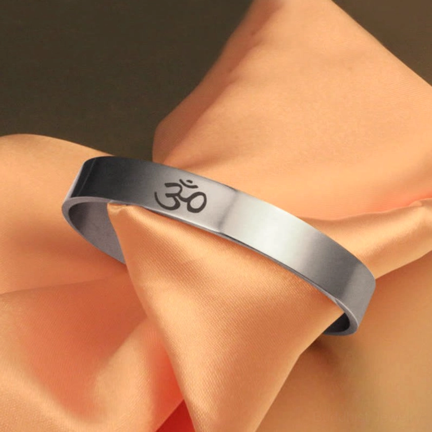 OM sacred symbol cuff bracelet draped on peach satin, three-quarter side view showing open cuff style