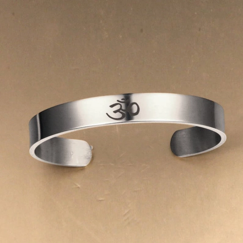 Spiritual OM engraved bracelet with bright polished silver, centered sacred symbol on neutral background