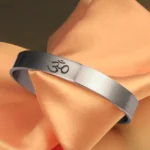OM symbol open cuff bracelet in polished silver, three-quarter front view on peach satin fabric